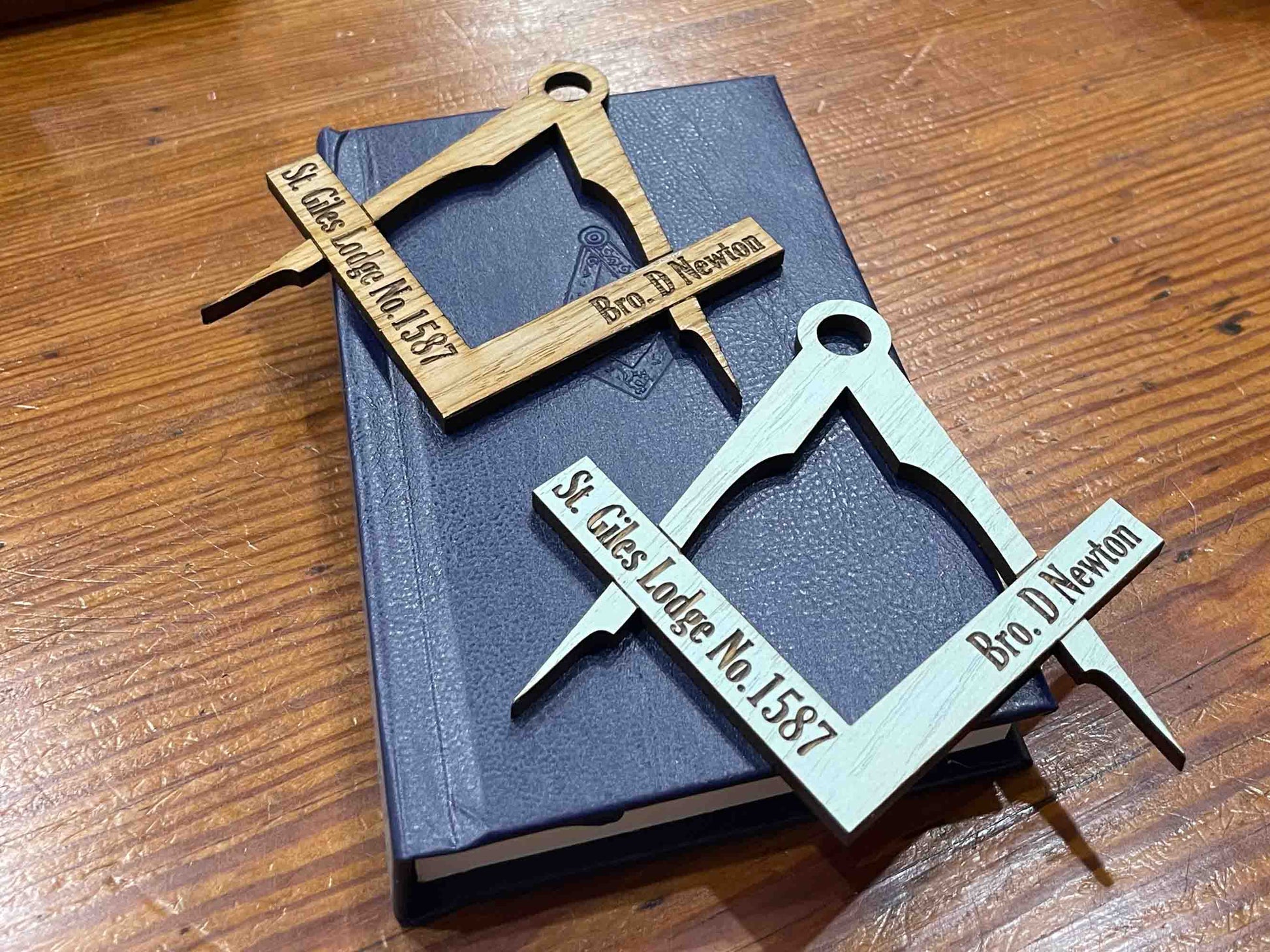 Image of a handcrafted oak table placename in the shape of a square and compass, with natural oak finish and engraved with details of the lodge and the person assigned to it.