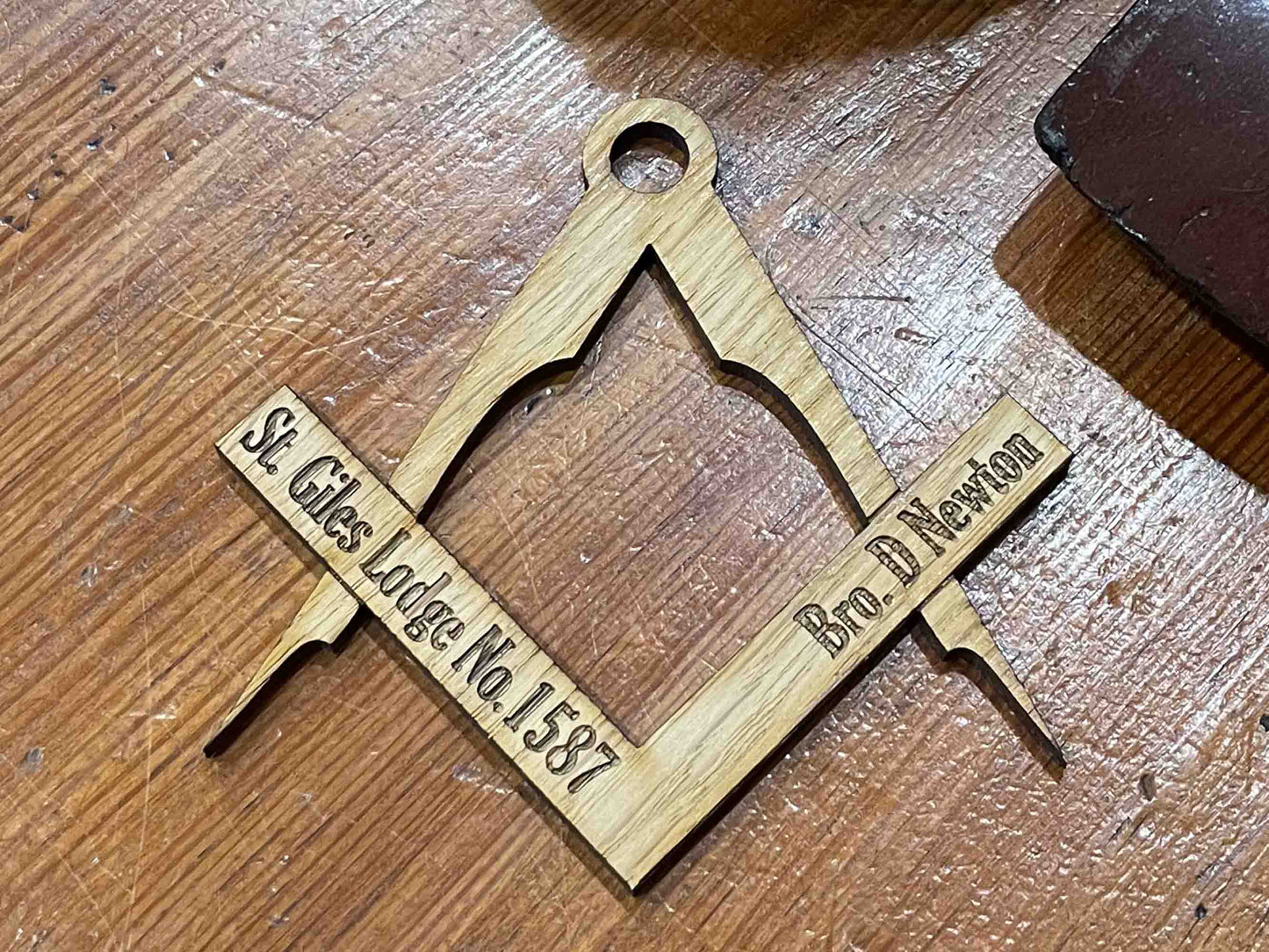 Image of a handcrafted oak table placename in the shape of a square and compass, with natural oak finish