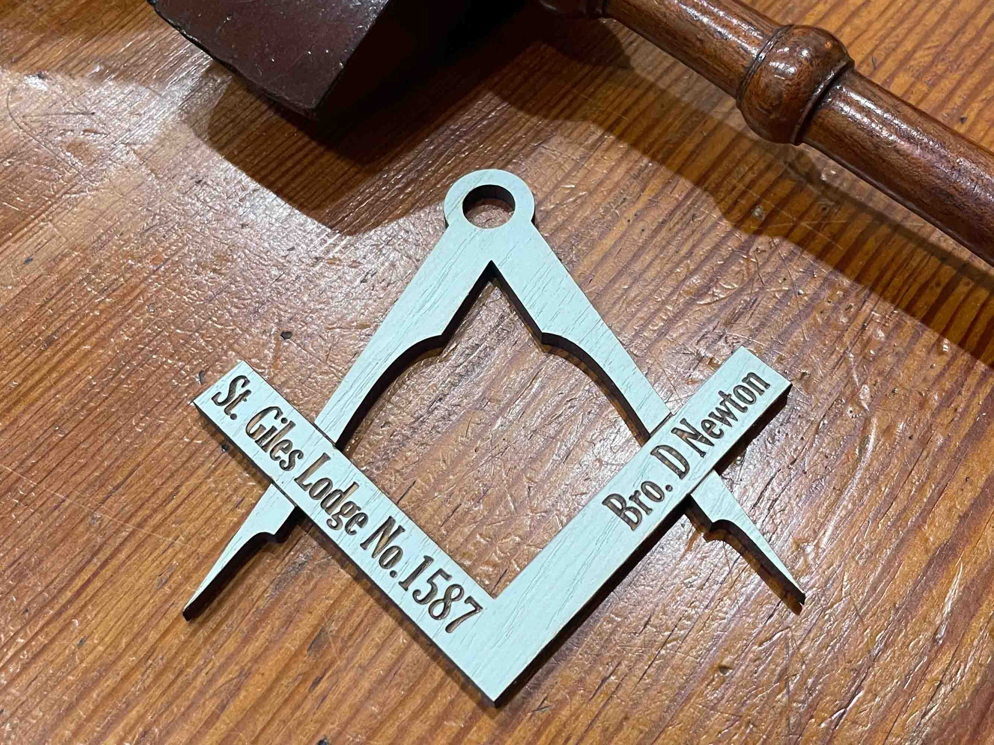 Image of a handcrafted oak table placename in the shape of a square and compass, hand painted light blue